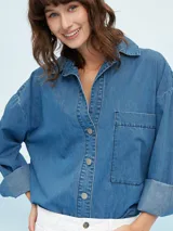 Camisa de denim azul de corte oversize, con mangas largas, cuello clásico, un bolsillo aplicado en el pecho y cierre frontal con botones metálicos.
