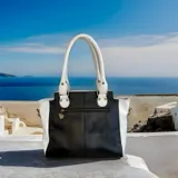 Cartera de cuero hecha a mano de la marca Carolina De Cunto, modelo Mila, con diseño tricolor en blanco, negro y detalle central dorado texturizado con arte pintado a mano. Cuenta con asas superiores blancas y herrajes metálicos.