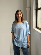 Blusa celeste de corte holgado, con cuello redondo, mangas tres cuartos con trabilla y detalles de alforzas en el frente.