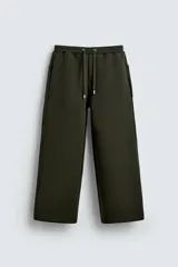Pantalón wide fit de tejido técnico con efecto neopreno, color verde oscuro. Presenta cintura elástica con cordón ajustable, perneras anchas con costura frontal, bolsillos laterales y bolsillos traseros de plastrón.