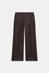 Pantalón de tiro medio en denim oscuro con costuras a contraste. Presenta corte recto, bolsillos delanteros, trabillas en la cintura y cierre frontal con cremallera y ganchos metálicos.
