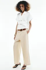 Pantalón culotte de tiro alto color beige, confeccionado con lino. Presenta pernera ancha y corta, bolsillos delanteros y falsos bolsillos de vivo en la espalda. Incluye un cinturón marrón con hebilla metálica redonda y cierre frontal con cremallera, botón interior y gancho.