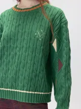 Sweater de punto con diseño de ochos en color verde, cuello redondo con detalle de franja en contraste, y apliques de rombos en las mangas. Presenta un bordado con la letra M en el pecho.