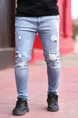 Pantalón jean chupín de corte ajustado, color celeste claro con roturas y desgarros en ambas piernas.