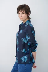 Camisa de corte clásico con cuello camisero y cierre frontal de botones, confeccionada en tela color bordó con estampado floral en tonos celestes.