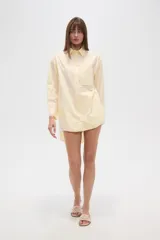 Camisa blanca de algodón, de corte holgado, con cuello camisero, botones frontales, un bolsillo de parche en el pecho y mangas largas con puños abotonados.