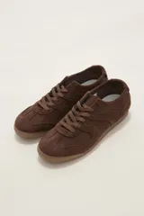 Zapatilla de estilo urbano confeccionada en gamuza color chocolate, con cordones al tono y suela de goma plana.