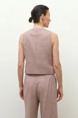 Chaleco de corte sastre con escote en V y cierre frontal con botones oscuros. Presenta un diseño de estampado a cuadros pequeños en tonos beige y rojizos.