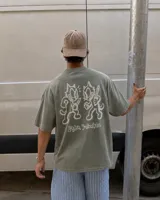 Remera marrón oversize de manga corta con estampado gráfico en la espalda de dos gatos de estilo retro con cuchillos y texto "Kahoa Industries".