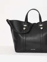 Cartera tipo tote Jazmín Chebar de cuero vacuno negro, con manijas superiores, correa regulable extraíble, acceso mediante imán y punteras metálicas decorativas.