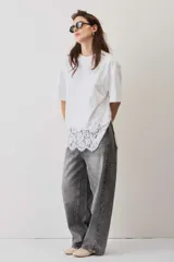 Remera blanca de algodón, de corte oversize, manga corta y cuello redondo, con detalle de aplique de encaje floral en el borde inferior.