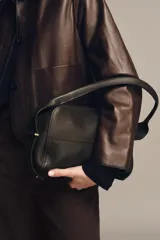 Bolso alargado de piel color marrón oscuro, con asa de hombro y cierre de cremallera. Incluye cartera con bolsillo extraíble.