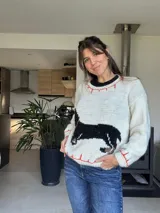 Sweater tejido color crudo, con cuello redondo y ribete naranja. Presenta un perro salchicha negro en el frente.