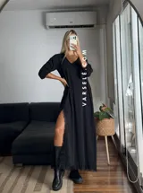 Vestido largo negro de tela de Cey, con escote en V, mangas largas abullonadas, tajo lateral con detalle de encaje y ruedo con encaje.