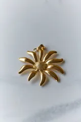 Collar con dije de acero quirúrgico en forma de flor tipo margarita, montado sobre un tiento de cuero negro.