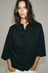 Camisa amplia confeccionada en hilatura con lyocell y ramio, color celeste, con cuello solapa, manga por debajo del codo, detalle de pliegue en la espalda y cierre frontal con botones ocultos por solapa.