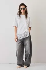 Remera blanca de algodón, de corte oversize, manga corta y cuello redondo, con detalle de aplique de encaje floral en el borde inferior.