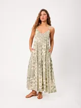 Vestido largo de algodón con estampado estilo patchwork en tonos verde y beige, escote en V con tirantes finos ajustables, diseño holgado y falda escalonada con bolsillos laterales.