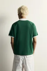 Polo de fútbol retro color verde oscuro, de corte regular fit, con cuello solapa blanco, mangas cortas con ribetes blancos y bandas en los hombros. Cuenta con estampado frontal del número 80 y un gráfico con efecto lavado.