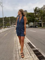 Vestido corto de jean azul, sin mangas, con cuello camisero, cierre frontal con botones y bolsillos en el pecho.