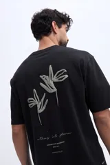 Remera oversize Brooksfield de color negro, confeccionada en 100% algodón, de manga corta y corte relajado. Cuenta con un diseño estampado en relieve en la espalda que representa flores abstractas y texto descriptivo en tono verde militar.