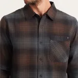 Camisa de franela a cuadros en tonos marrón, gris y azul, de manga larga, con cuello clásico, cierre frontal con botones, bolsillo de parche en el pecho y corte recto.
