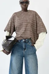 Remera oversize de manga corta superpuesta a una manga larga, ambas de algodón. La capa superior es marrón con rayas horizontales finas en blanco y presenta un efecto lavado. La capa inferior es de color crema o blanco roto.