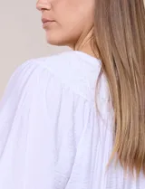 Blusa blanca de rayón y poliéster con textura, escote en V y delicados bordados al tono sobre el canesú. Cuenta con mangas raglán tres cuartos abullonadas con puños elastizados y diseño holgado.