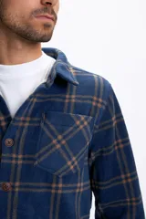 Sobrecamisa de polar a cuadros en tonos azul marino y marrón, con interior forrado en corderito, cierre frontal de botones, cuello clásico y bolsillos frontales en el pecho.