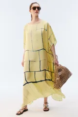 Kaftan maxi amplio de color amarillo, con escote redondo, mangas cortas y ruedo irregular. Presenta un diseño estampado a cuadros con efecto teñido.