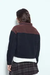 Campera de jean color negro con cuello de pana en tono marrón, cierre frontal con botones y bolsillos en el pecho. Presenta un diseño de corte relajado y ligeramente cropped, con interior forrado en corderito para mayor abrigo.