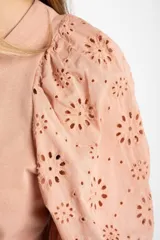 Remera de algodón color rosado con mangas cortas abullonadas de broderie con diseño floral calado. Presenta cuello redondo y costura vertical central en el frente.