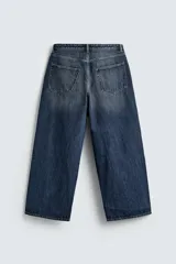 Jeans de denim de algodón, color azul oscuro con efecto lavado. Presentan un corte muy holgado (baggy fit) en toda la pierna y tiro medio. Tienen cinco bolsillos y cierre frontal con cremallera y botón.