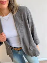 Blazer de lino color beige, de corte relajado y líneas clásicas. Presenta cuello con solapas, cierre frontal con dos botones y bolsillos con solapa en el frente.