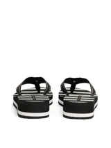 Ojotas de mujer con plataforma tipo cuña, suela EVA dentada y tiras de textil trenzado a rayas negras y blancas. Presentan una insignia con monograma TH en la tira del dedo.