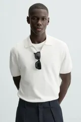 Jersey de punto color verde oliva, de calce relajado (relaxed fit), con cuello solapa y abertura frontal en forma de V. Es de manga corta y presenta acabados en rib en puños y ruedo.