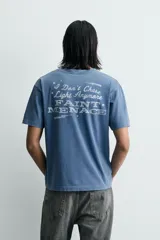 Camiseta relaxed fit de color azul con efecto lavado, cuello redondo y manga corta. Cuenta con un estampado de texto a contraste en el delantero y acabados con efecto rotos.