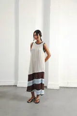 Vestido midi de punto color crema, con cuello redondo y sisas ribeteadas en negro. Presenta un panel horizontal marrón a la altura de las rodillas, seguido de un panel con calados horizontales en marrón y celeste.