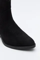 Bota corta estilo western de gamuza color marrón, con taco cuadrado negro y puntera estilizada. Presenta un detalle de estrella aplicada en el lateral y tirador en la parte superior.