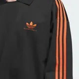 Camisa polo Adidas de manga larga en color negro, con cuello clásico y las icónicas tres tiras naranjas en las mangas. Presenta el logotipo del trébol bordado en naranja en el pecho con la inscripción 'Basketball'.