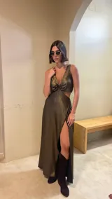 Vestido largo de fiesta con escote en V profundo y detalle de aro central. Presenta aberturas laterales en la cintura y falda con tajo frontal y diseño en capas diagonales. Confeccionado en tela con acabado brillante.