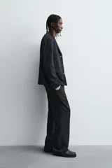 Pantalón de corte relaxed fit confeccionado en tejido con mezcla de lana, con bolsillos delanteros y traseros de vivo, cierre frontal con cremallera y botón.