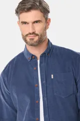 Camisa azul de pana fina con cuello camisero, bolsillo frontal en el pecho y cierre de botones marrones.