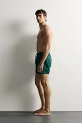 Short de baño confeccionado en tejido técnico, con diseño de rayas verticales en color verde y negro. Cuenta con cintura elástica ajustable con cordón, bolsillos laterales y bolsillo trasero con vivo, además de forro interior.