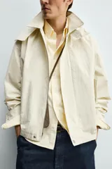 Parka cropped fit de tejido técnico ligero color beige, sin forro interior, con cuello solapa, capucha desmontable y manga larga. Cuenta con bolsillos de solapa en la cadera y cierre frontal con cremallera oculta por solapa con botones a presión.