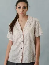 Camisa de pijama de manga corta color beige con estampado de letras negras, cuello clásico y cierre frontal con botones.
