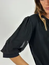 Blusa negra de manga 3/4 con cuerpo de algodón liso y mangas abullonadas de tejido transparente y arrugado.