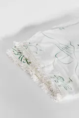 Pareo de playa blanco con estampado de hojas verdes y borde de encaje con flecos.