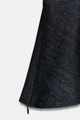 Blusa de denim oscuro con escote en pico, mangas cortas abullonadas y diseño peplum con bajo evasé. Presenta cierre frontal con alamares decorativos y cierre lateral con cremallera oculta.