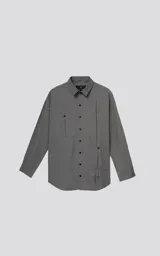 Camisa manga larga de corte oversize, confeccionada en twill color gris melange. Presenta cuello clásico, cierre frontal con botones y tres bolsillos delanteros, uno de ellos oculto.